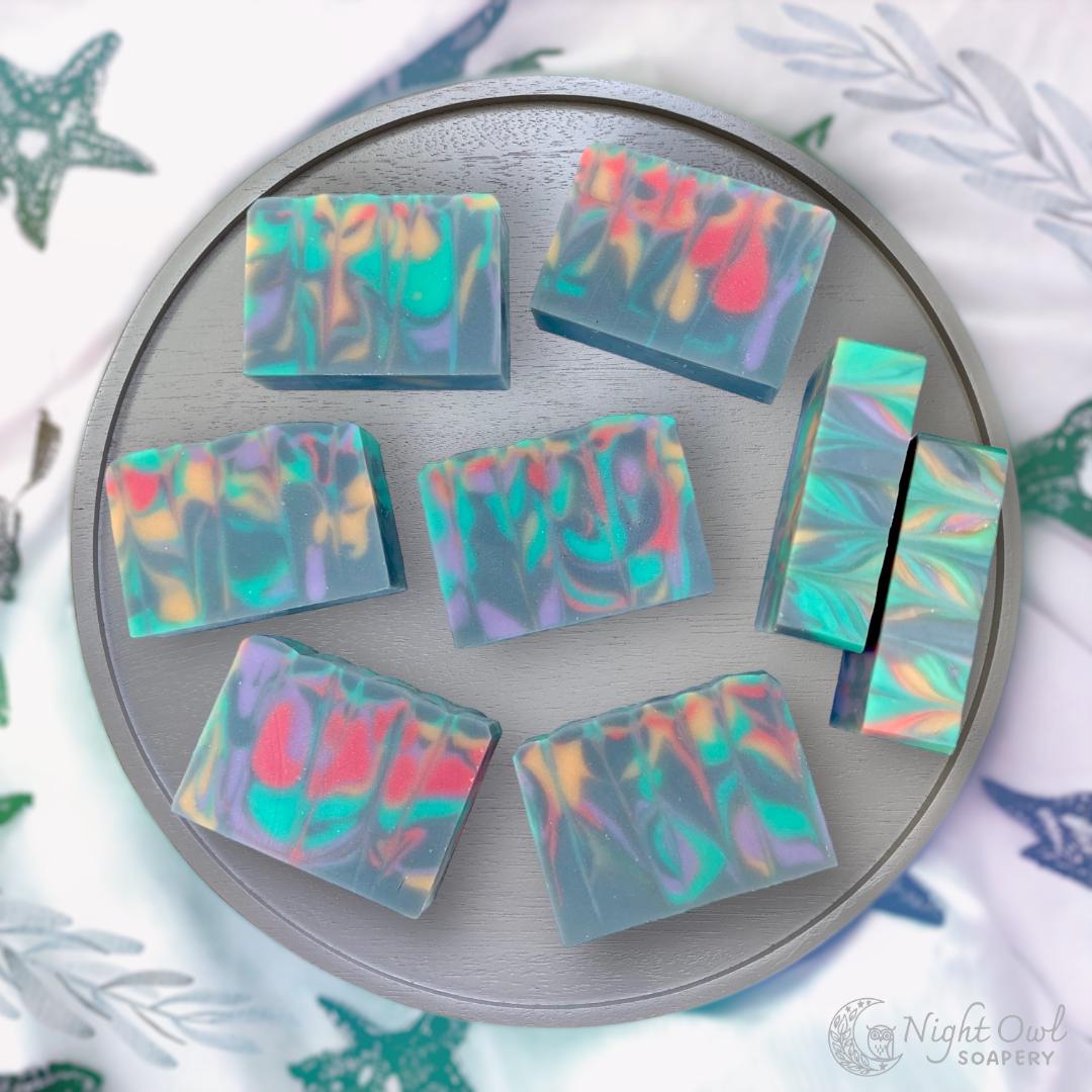 Colorful soap bars on a round gray wooden tray with a white beach pattern fabric background