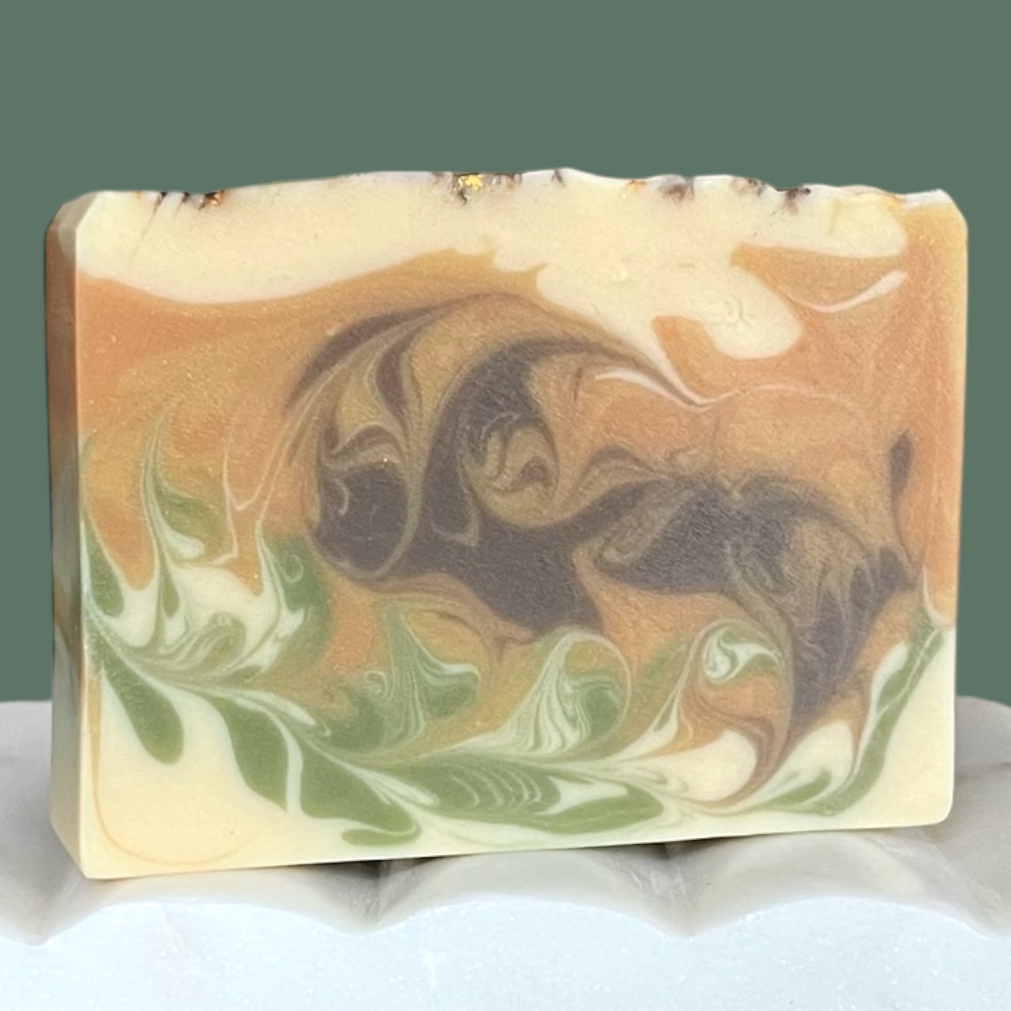 Swirled soap bar with gold, brown, green, and white colors on a white background