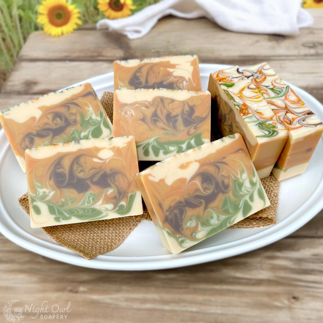 Handmade soap bars with marbled design on a white plate, set on a wooden table with sunflowers in the background.