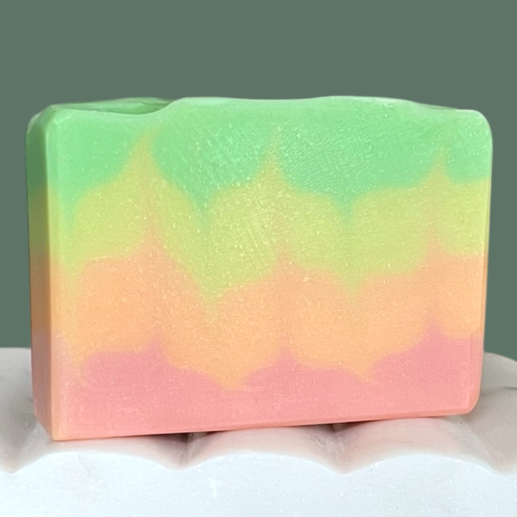 Colorful soap bar with green, yellow, orange and pink layers on a white surface.