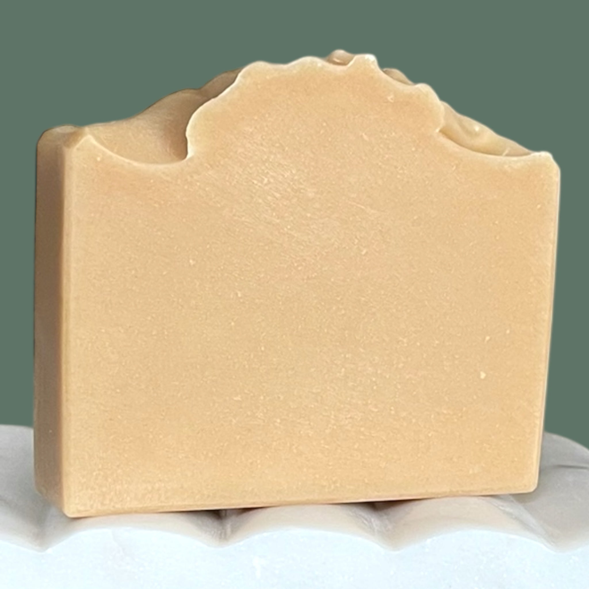 Beige bar of soap on a white surface with a green background