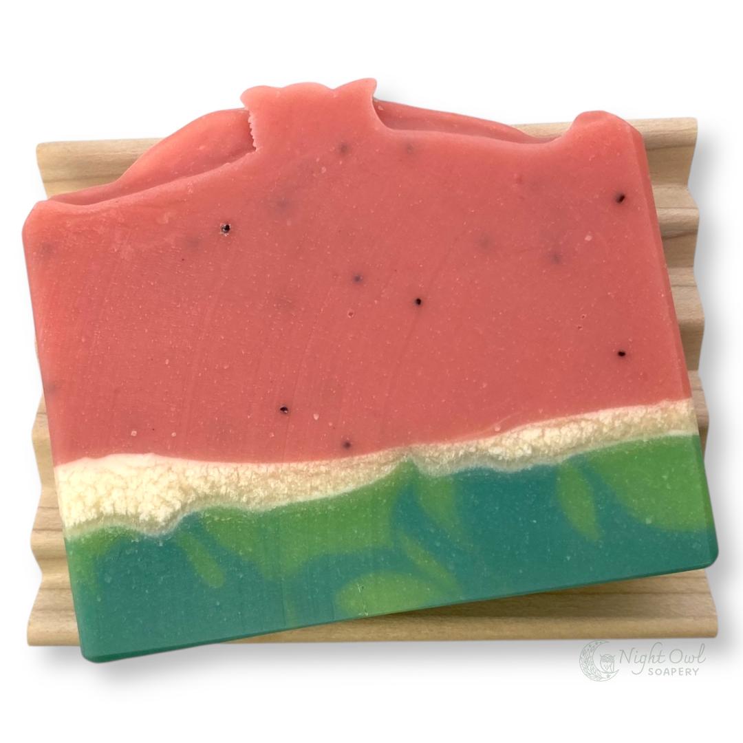 Colorful layered realistic watermelon soap bar on a wooden block with a white background