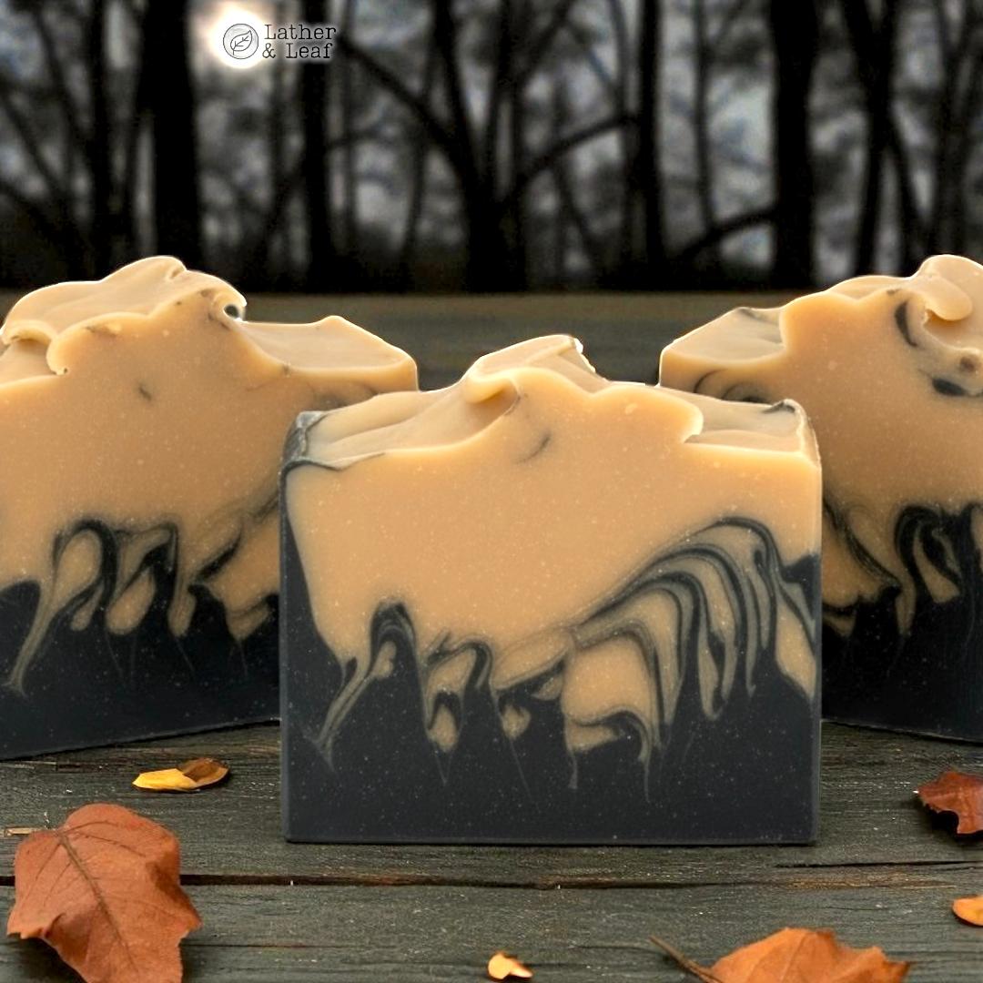 Three bars of soap with black and white swirls on a wooden surface with autumn leaves.