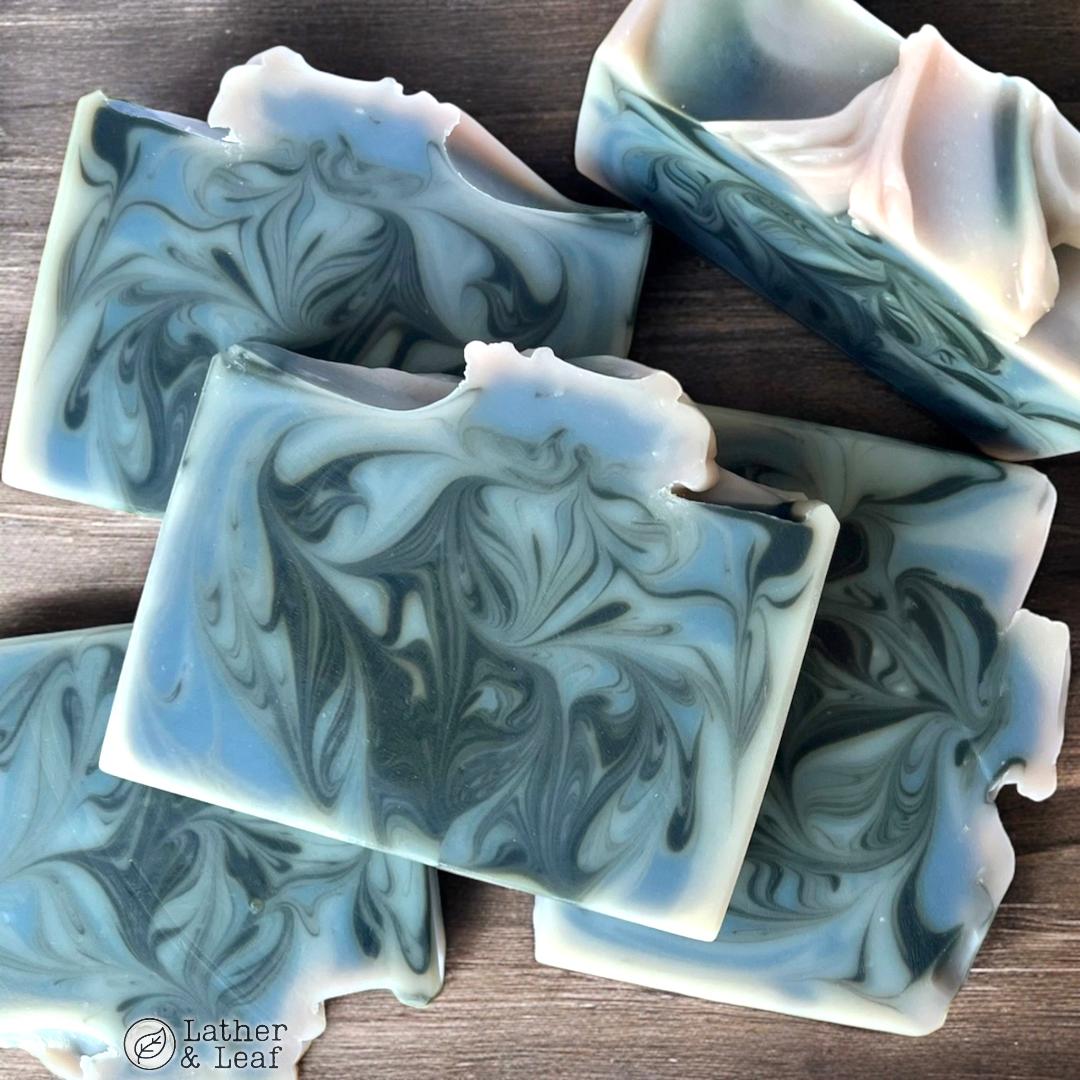 blue, light purple and black swirled soap bars on a wooden surface with 'Lather & Leaf' branding.