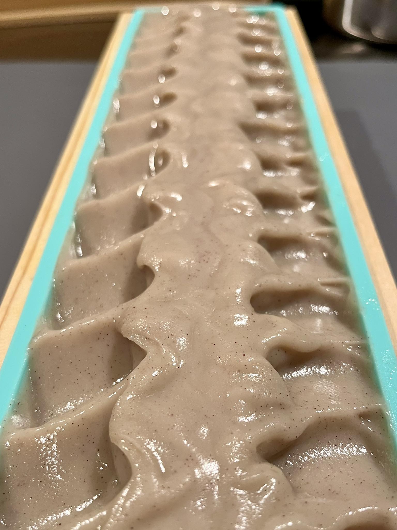 Close-up of a rectangular soap mold filled with freshly poured blueberry and oats soap inside