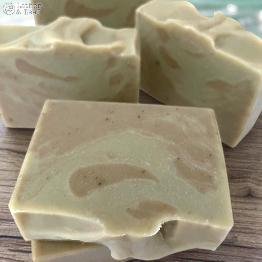 Three bars of soap with a beige and light green marbled pattern on a wooden surface