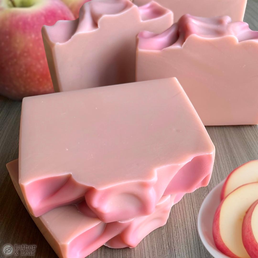 Pink soap bars with textured tops on a wooden surface with apples.
