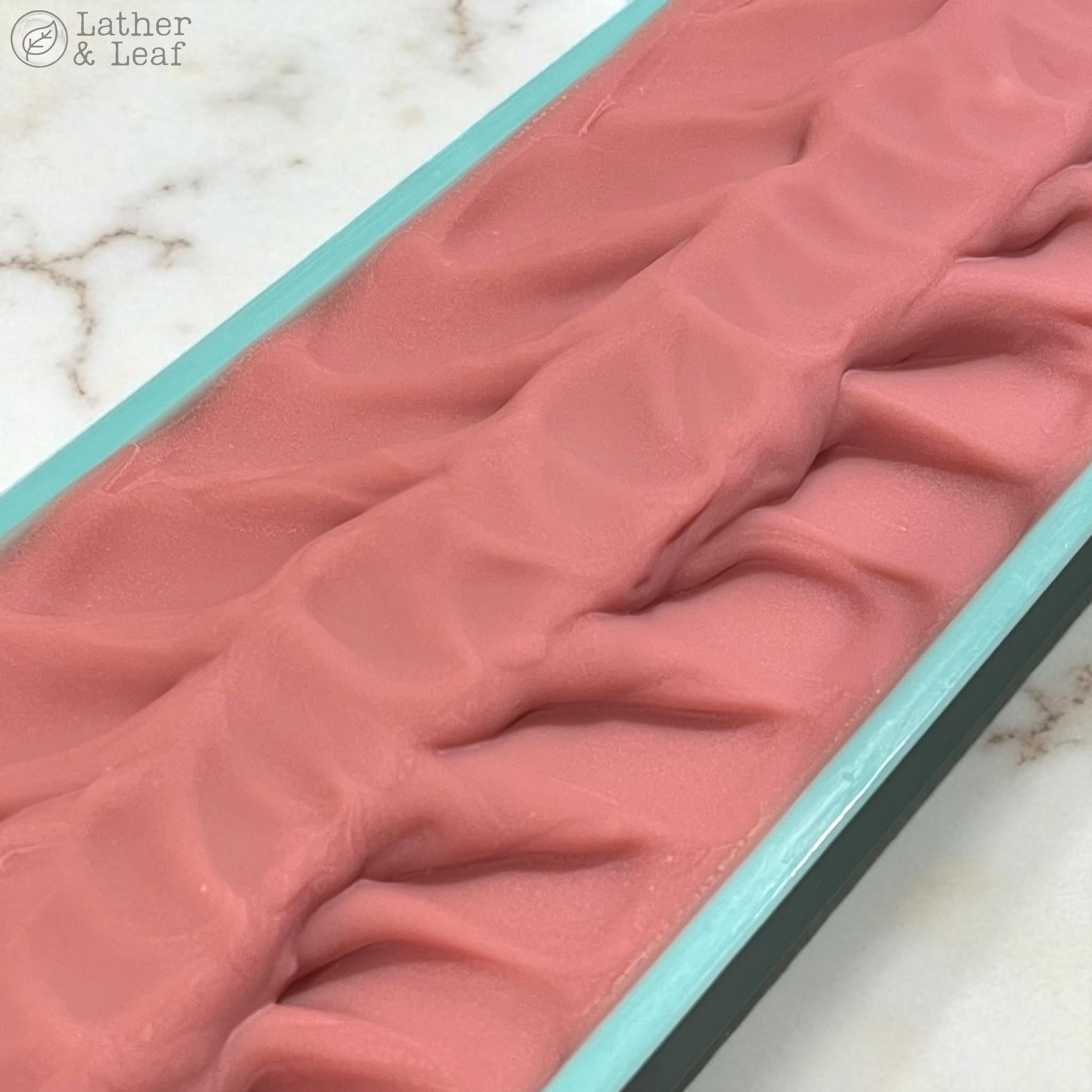 Pink soap loaf still in a mold on a marble surface 