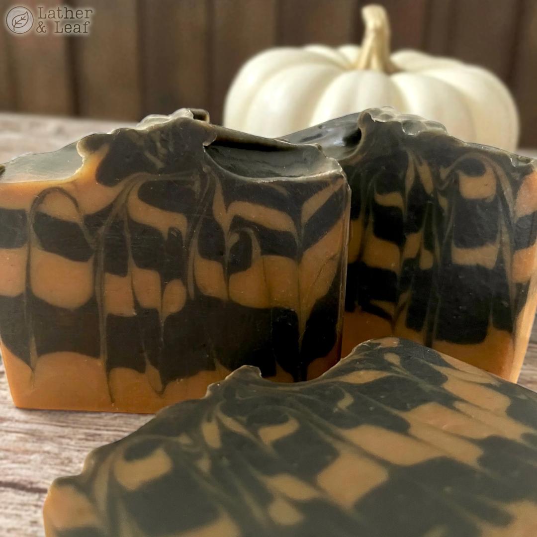 pumpkin and charcoal soap bars close up photo on a table with a white pumpkin in the background