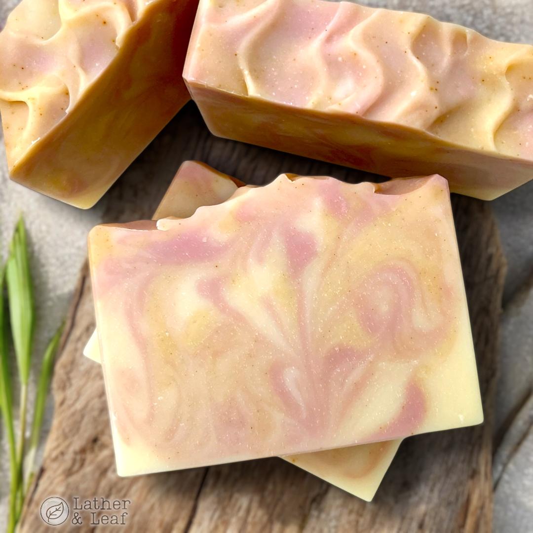 A photo of bars of handcrafted soap with a swirled pattern of pink and yellow tones, set on a wooden surface.